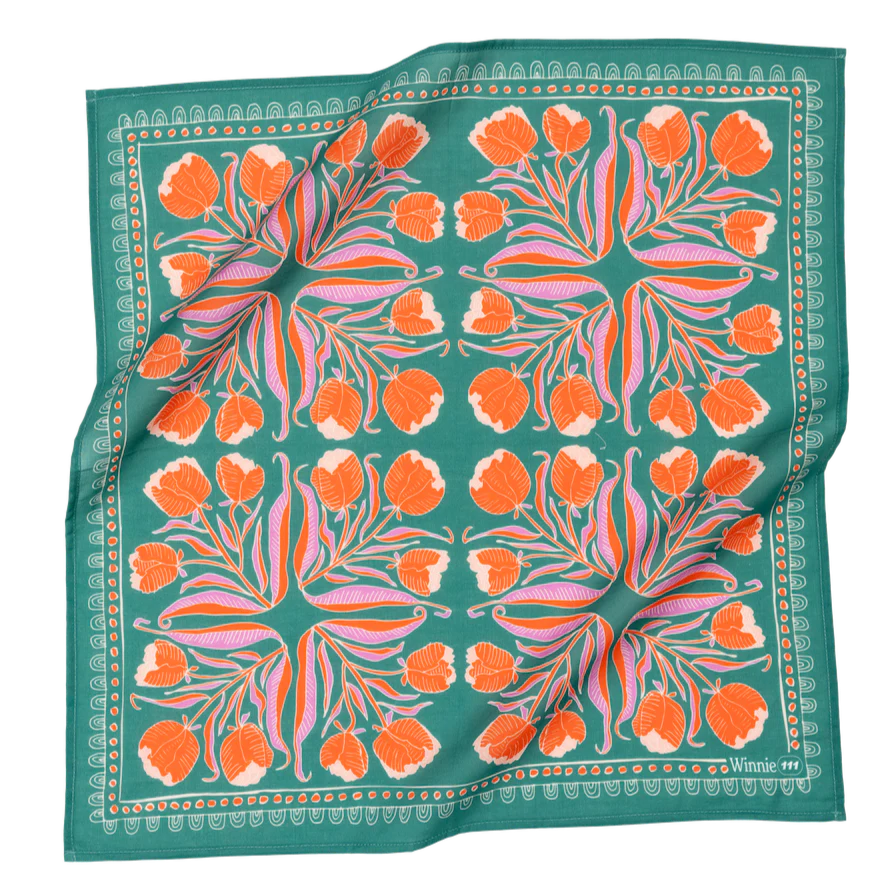 This image showcases a **square fabric bandana** with a **bold and intricate floral design** set against a rich **teal green background**. The symmetrical pattern features **vibrant orange flowers, flowing pink and purple leaves, and delicate white accents**, creating a striking and artistic composition. A decorative border with geometric elements frames the design, adding a refined touch. The bandana appears to be made from a lightweight fabric, making it a versatile accessory for wearing as a **headscarf,