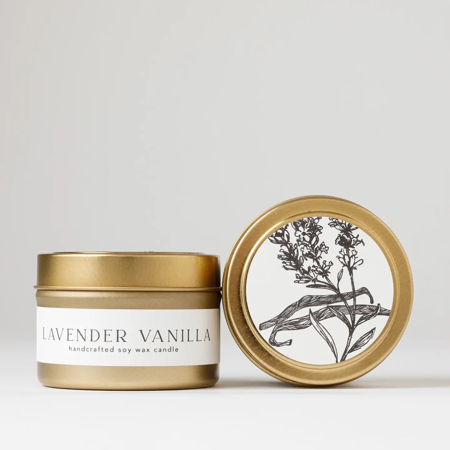 Gold tin soy wax candle labeled “Lavender Vanilla,” with one lid showing a botanical illustration of lavender and vanilla on a white background.