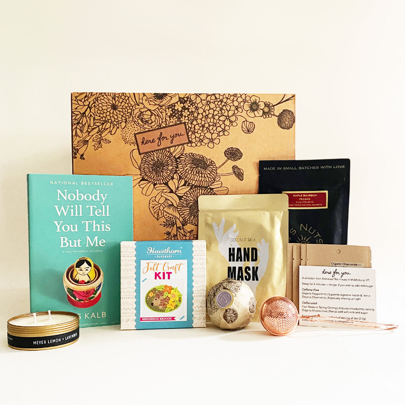 This **Here For You** care package is a beautifully curated collection of comforting items, perfect for someone experiencing grief or in need of self-care. It includes a **bestselling book ("Nobody Will Tell You This But Me")**, a **felt craft kit**, **hand mask**, **artisan snacks**, **tea with a strainer**, a **scented candle**, and **bath products**. Thoughtfully packaged in a floral-designed box, this gift offers **warmth, support, and gentle encouragement**.