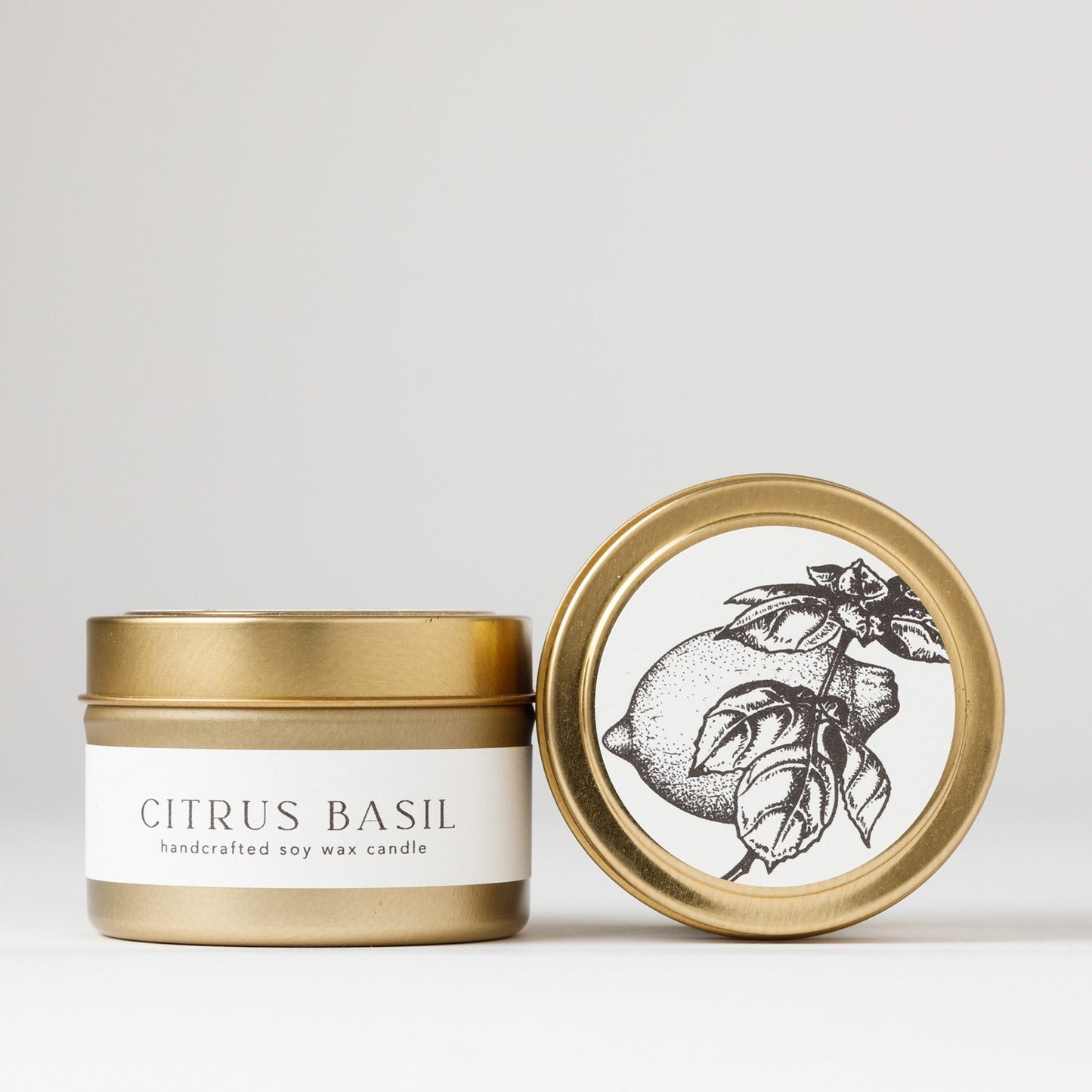 Gold tin soy wax candle labeled “Citrus Basil” with one lid showing a botanical illustration of a lemon and basil on a white background.