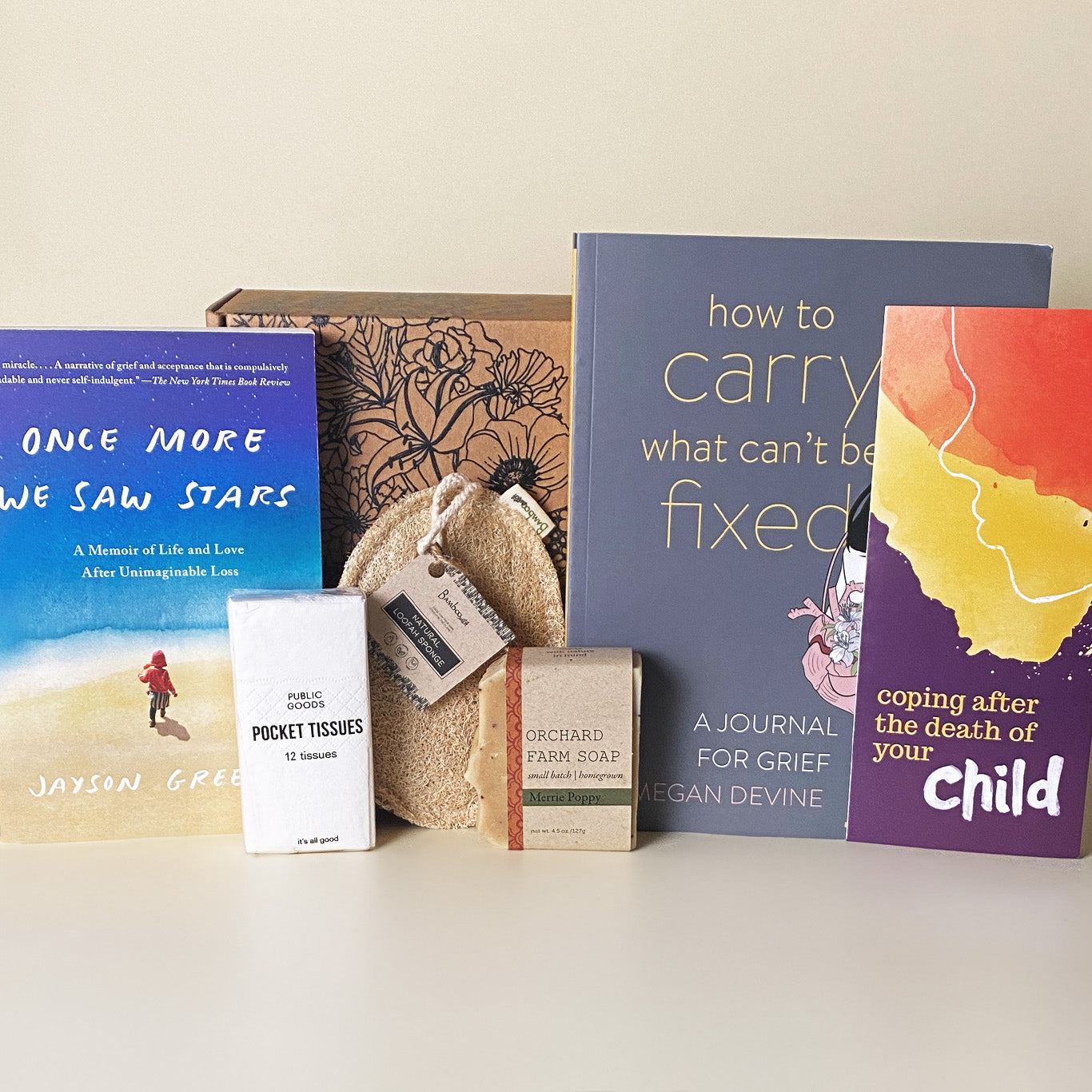A child loss grief care package including the books Once More We Saw Stars, How to Carry What Can’t Be Fixed, and the brochure Coping After the Death of Your Child, along with pocket tissues, a natural loofah, Merrie Poppy handmade soap, and a floral box.