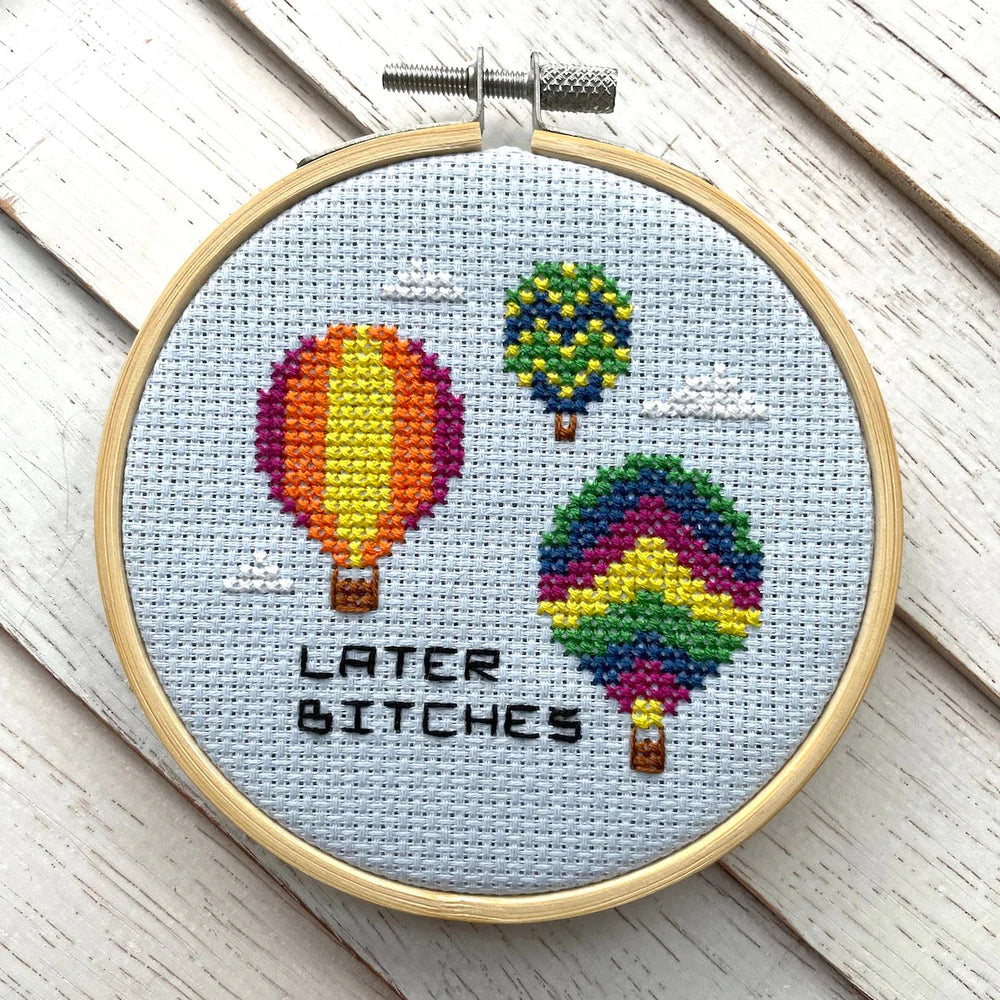 Cross-stitch hoop featuring hot air balloons with the phrase “Later bitches” stitched in black on a light blue background.