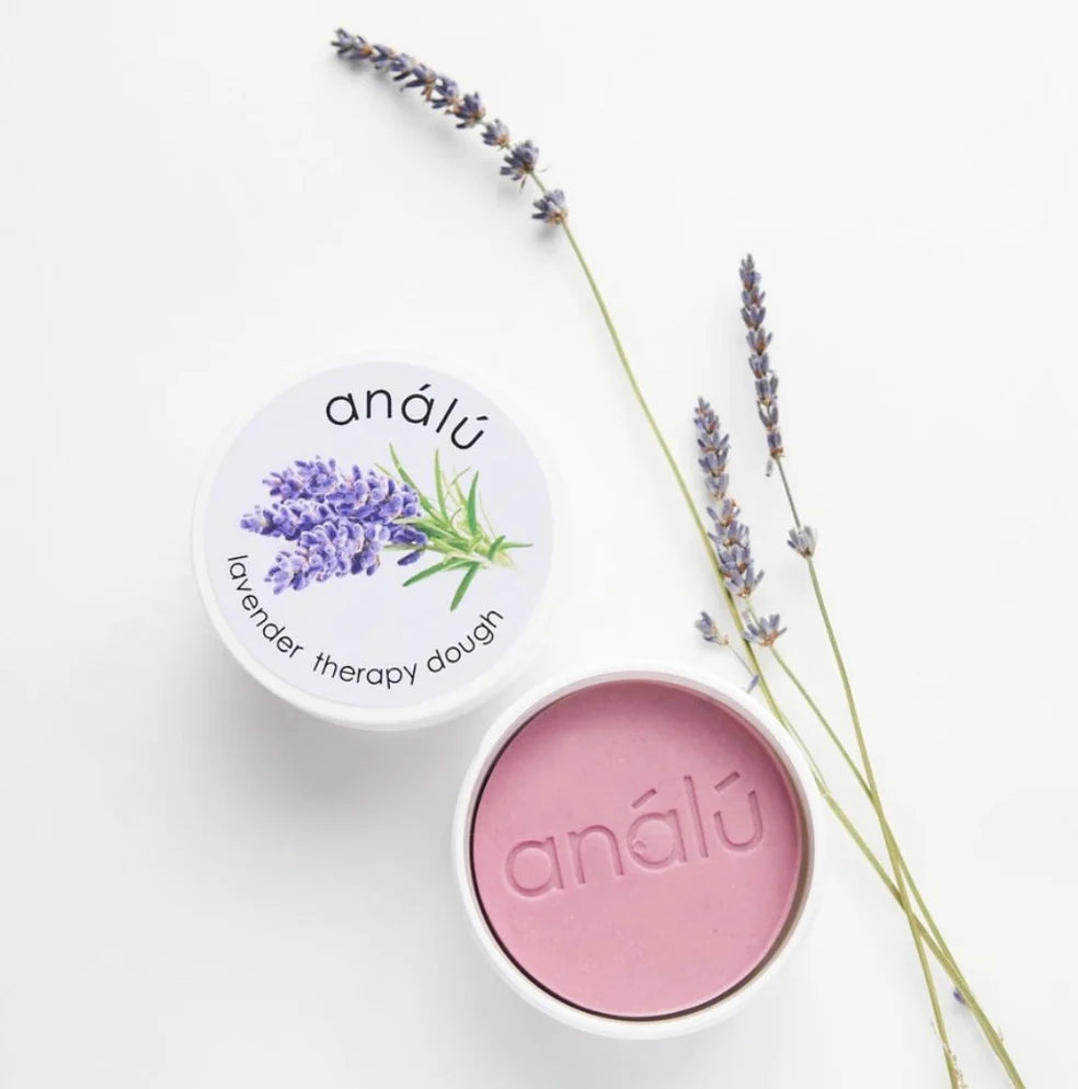 This image showcases **Análú Lavender Therapy Dough**, a calming sensory tool designed to help with **stress relief and relaxation**. The dough is a soft, **lavender-infused** putty housed in a sleek white container, featuring a delicate **lavender illustration on the lid**. Accompanied by sprigs of dried lavender, the image conveys a sense of **tranquility and self-care**, making it a perfect **aromatherapy aid for grounding and mindfulness**.