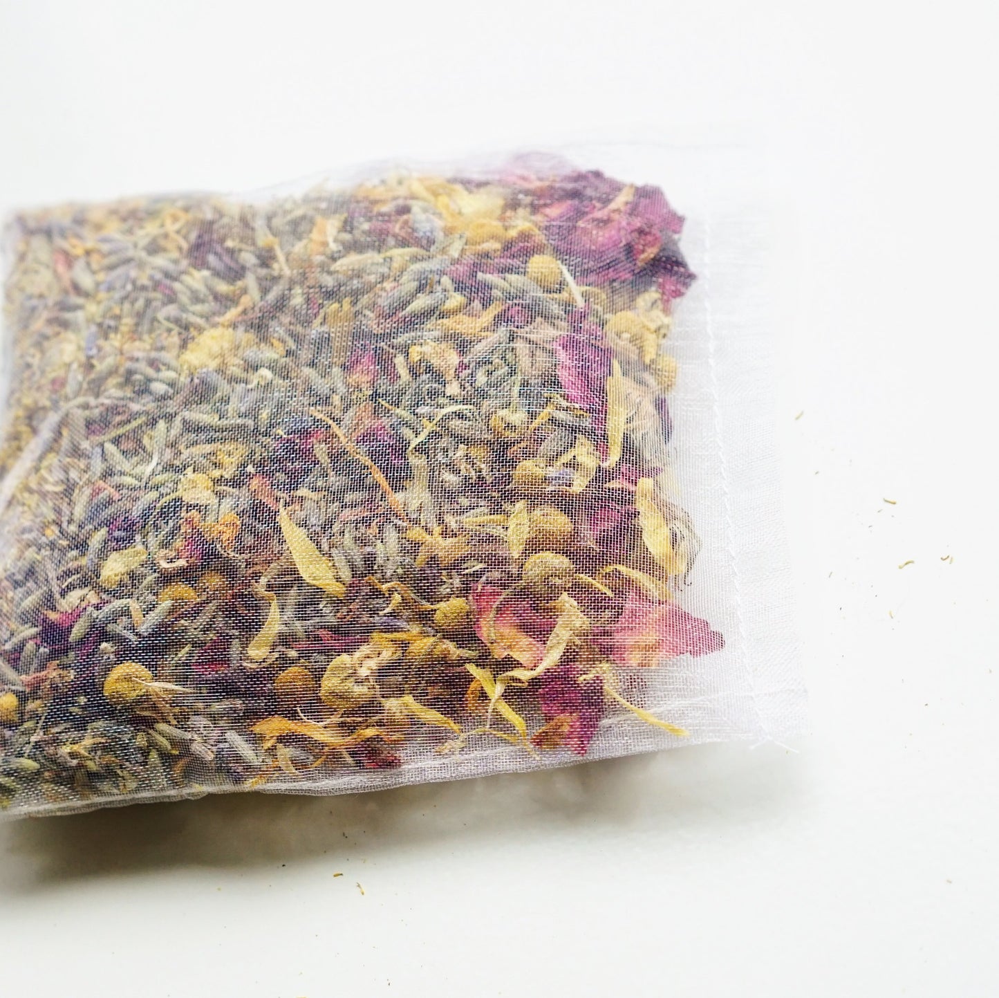 This image features a **close-up of a herbal bath tea sachet** filled with a blend of **dried botanicals, including lavender, chamomile, and rose petals.** The fine mesh bag allows the herbs to infuse into bathwater, creating a **soothing, aromatic experience** for relaxation and skincare. Ideal for **stress relief, muscle relaxation, and self-care rituals**, this bath tea is a natural alternative to bath salts or bubble baths.
