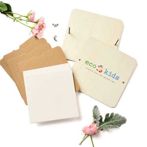 A flower press kit by Eco-Kids includes wooden covers, cardboard layers, blank paper sheets, and metal bolts for assembly. Surrounded by pink flowers and leaves, it encourages kids to press and preserve plants naturally.