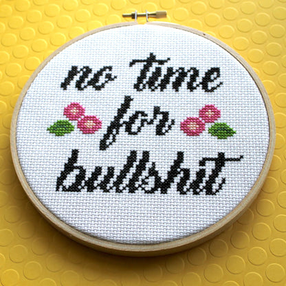 Cross-stitch that reads “no time for bullshit” with pink flowers on a yellow background.