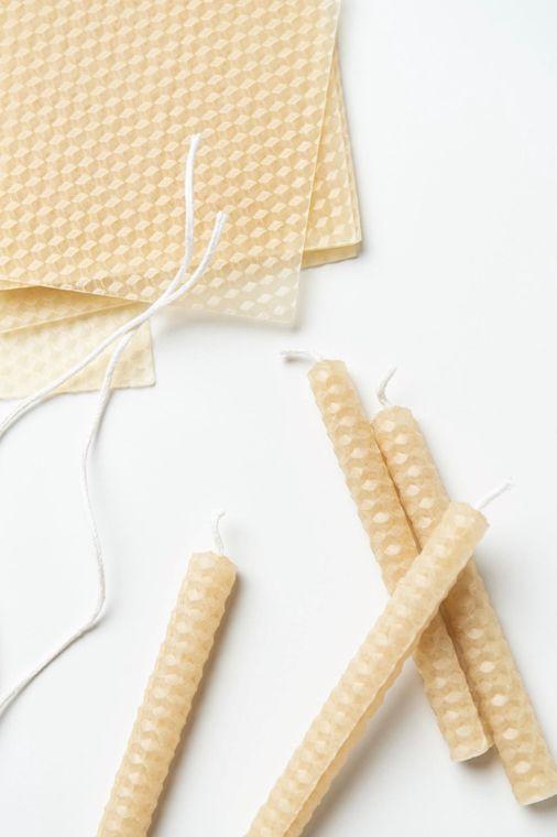 This image showcases **hand-rolled beeswax candles** made from **honeycomb-textured beeswax sheets**. The natural wax sheets are accompanied by **cotton wicks**, ready for crafting into **eco-friendly candles**. The scene highlights both the process and finished candles, emphasizing a **sustainable and DIY approach** to candle-making.